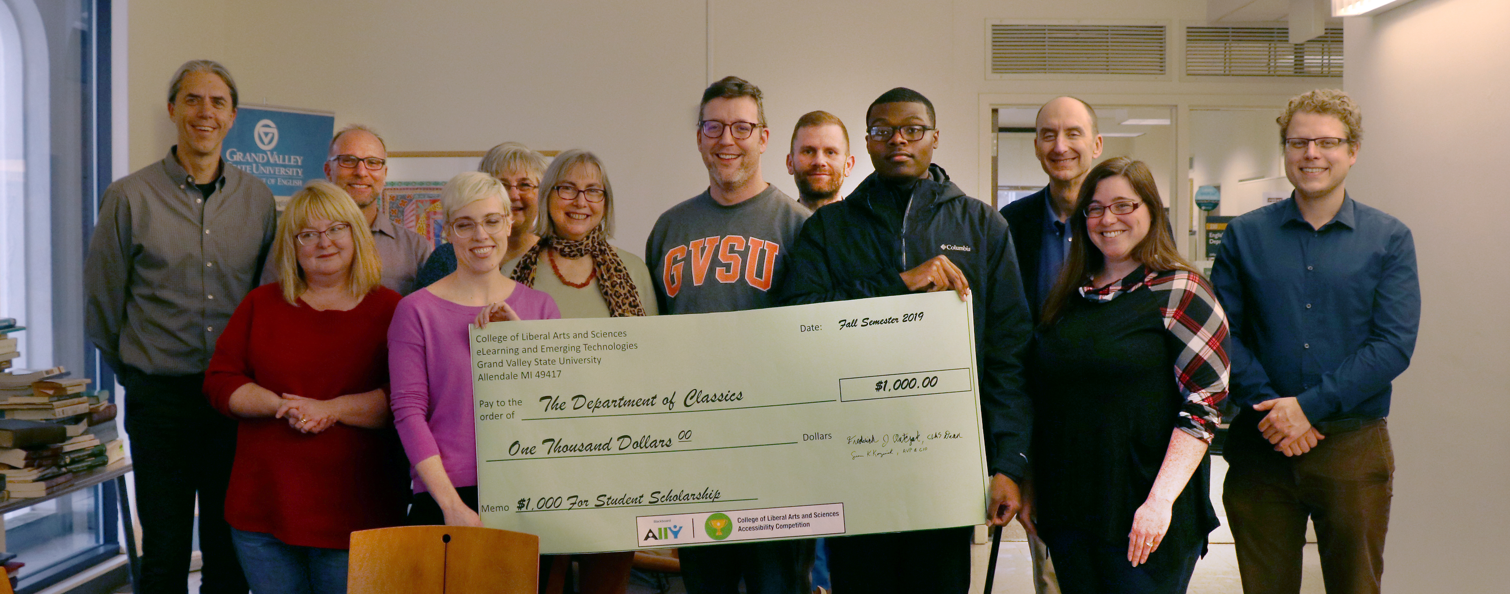The department of classics staff are pictured holding a large poster check with a total amount of $1,000. The memo of the check is labeled: $1,000 For Student Scholarship.